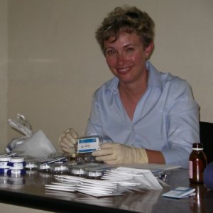 A photo of Connie Mulligan handling samples at the Mulligan Laboratory. She is wearing a light blue button down shirt and smiling at the camera. 